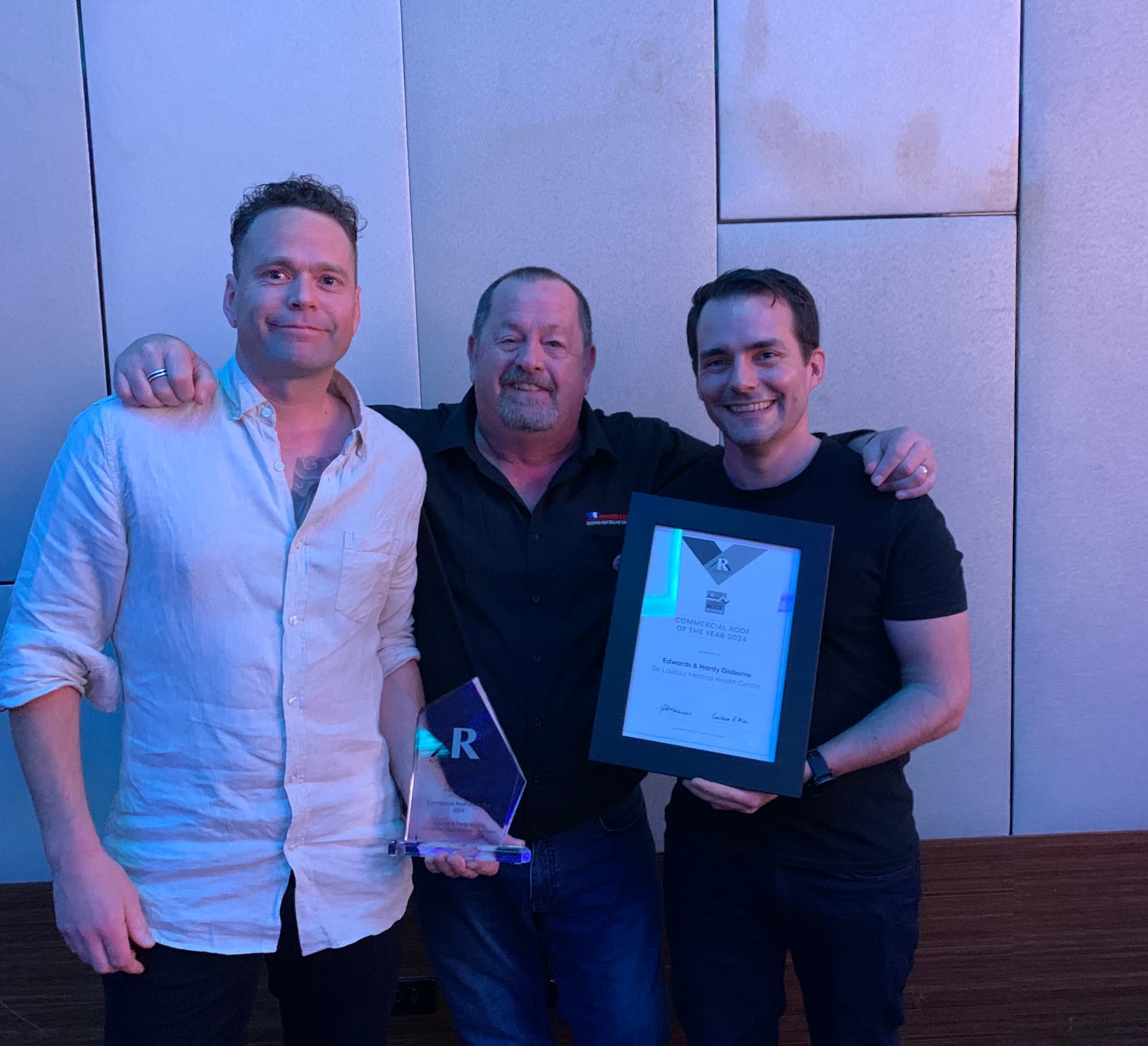 Three men standing proudly with an award in front of a wall.