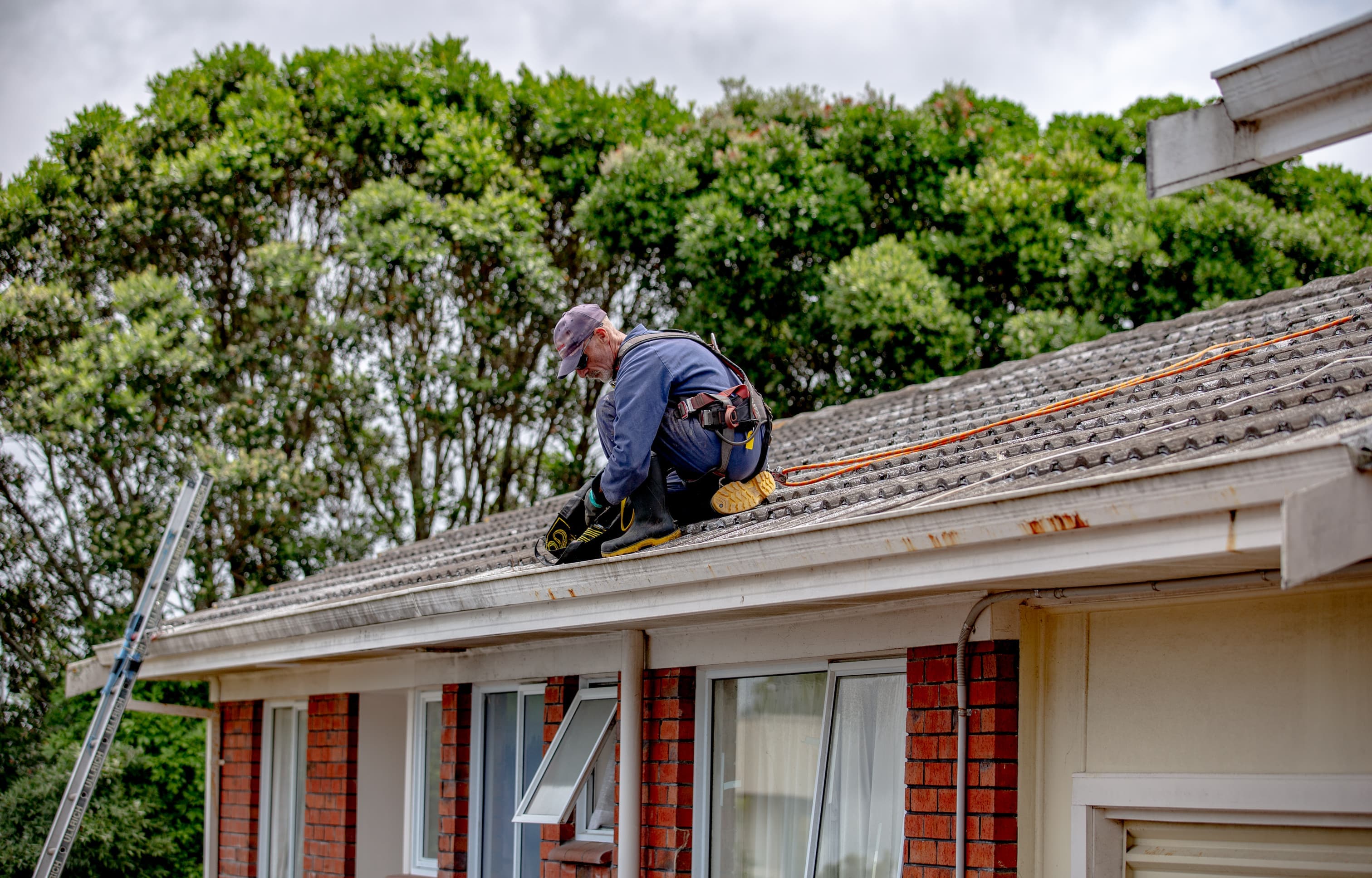 Person on roof with harness clearing a blocked gutter