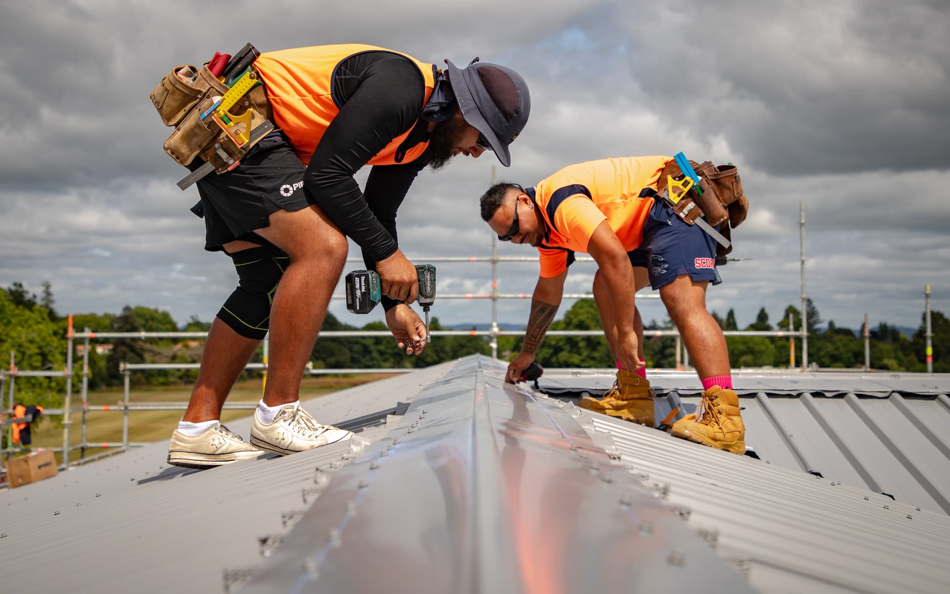 Edwards & Hardy roofers on scaffolding installing metal roofing sheets on one of the Fairfield College buildings under a stormy sky