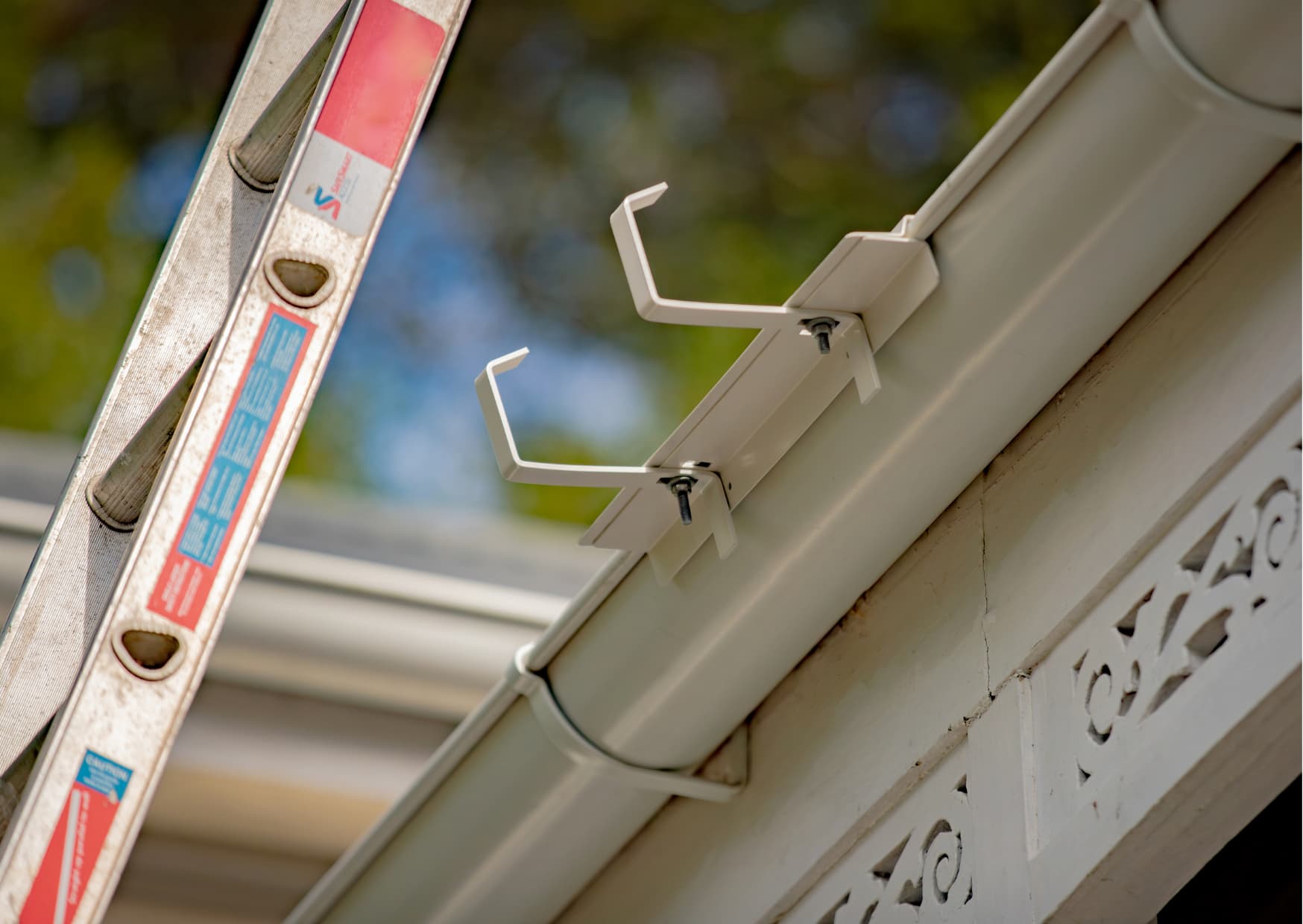 Person on a ladder using a hose to clean gutters on a residential New Zealand home