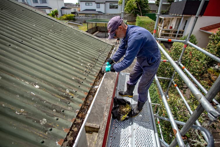 Person cleaning a gutter on scaffolding