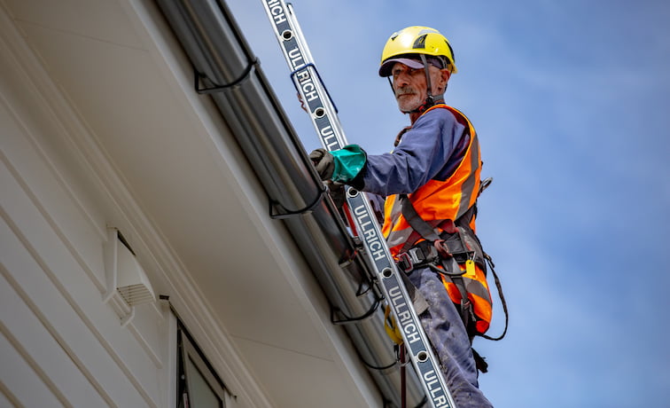 Person cleaning a gutter off a ladder
