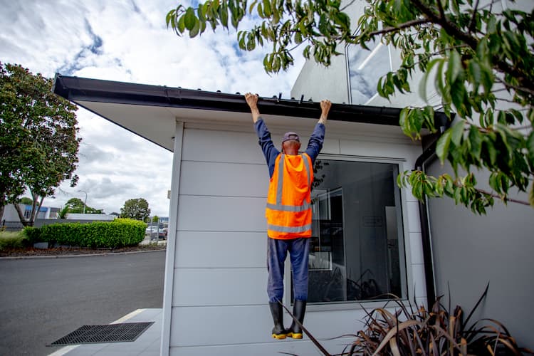 A man hanging off a building's side, gripping onto the gutter for support.