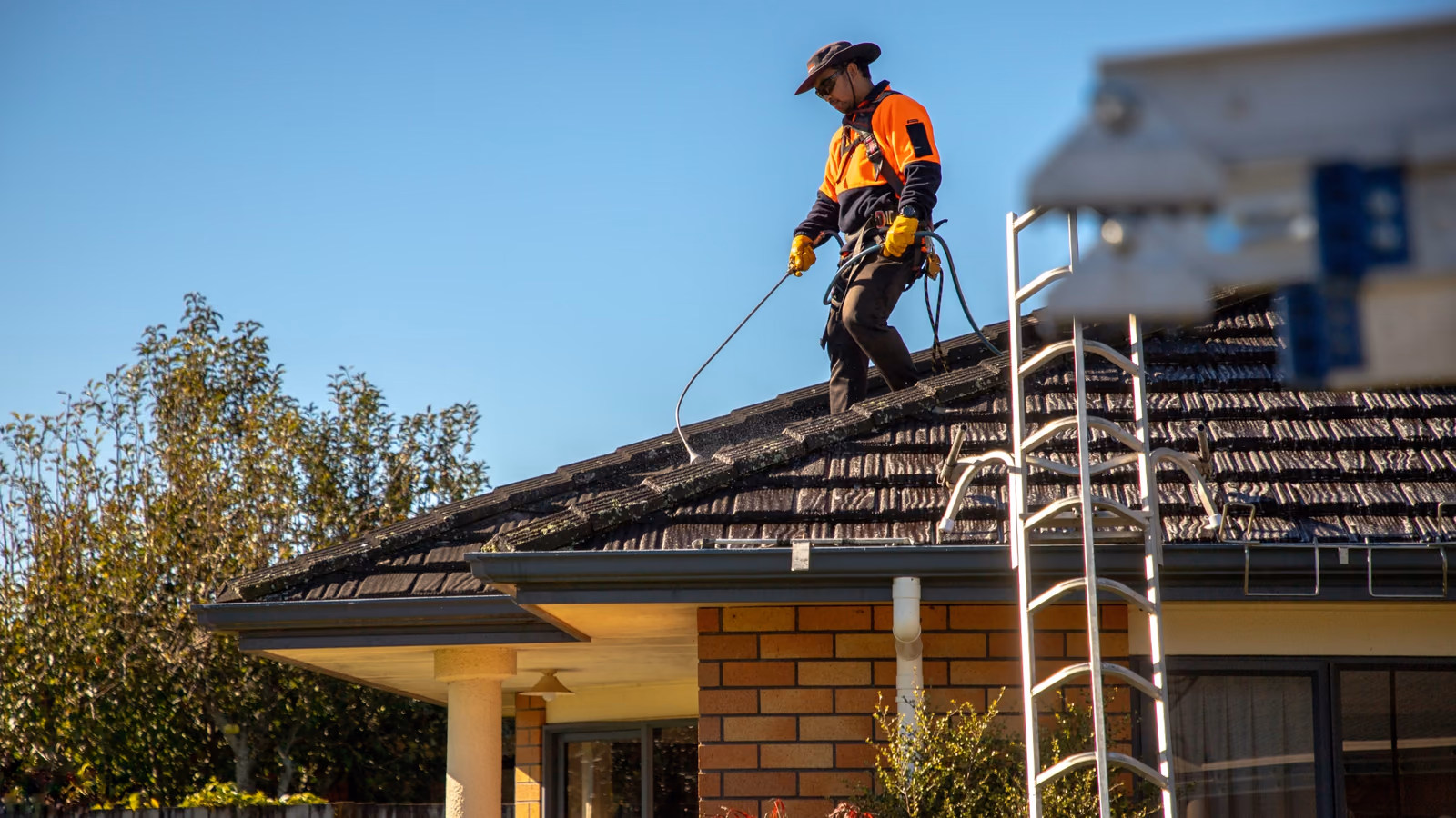 Professional roof specialist applying moss treatment to a tiled roof in New Zealand