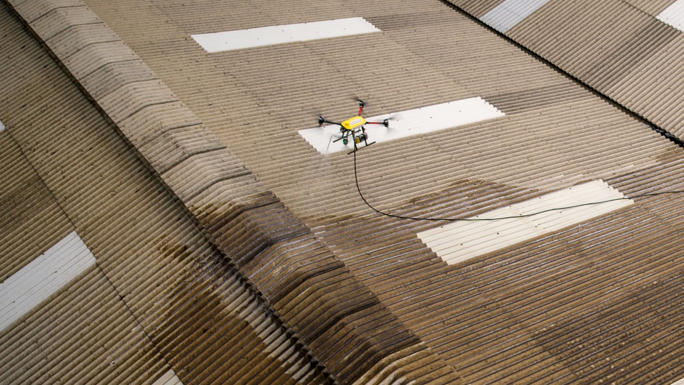 Tethered drone applying treatment across a large asbestos roof at Gallagher in Pukekohe