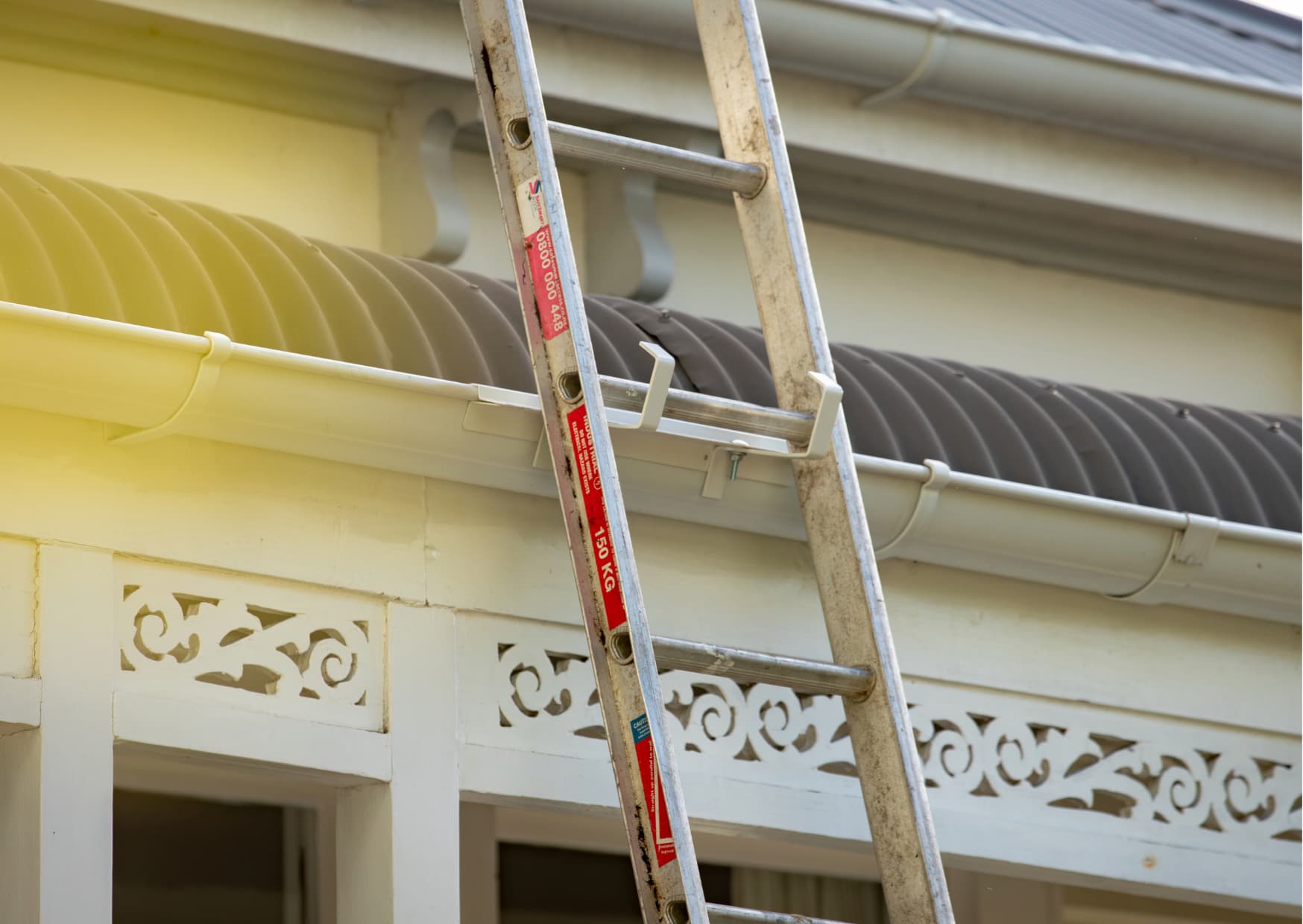 Close-up of a Ladder Secure bracket screwed onto a white gutter with a ladder resting against it