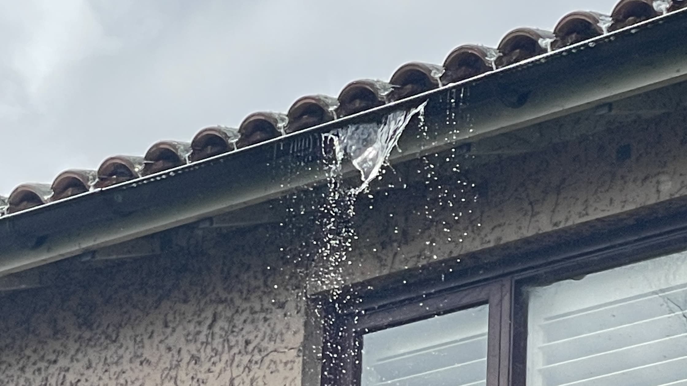 Water overflowing from a residential gutter during heavy rain above a window